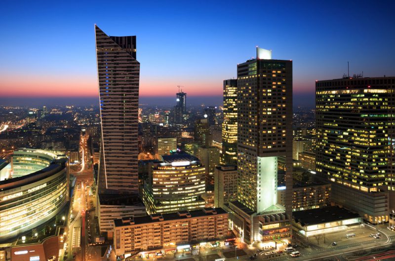 widok z lotu ptaka na centrum Warszawy oświetlone nocą, w tle wysokie wieżowce