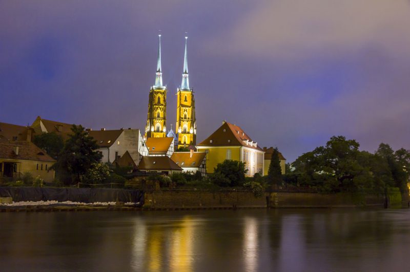 widok z brzegu rzeki na oświetlony nocą kościół we Wrocławiu