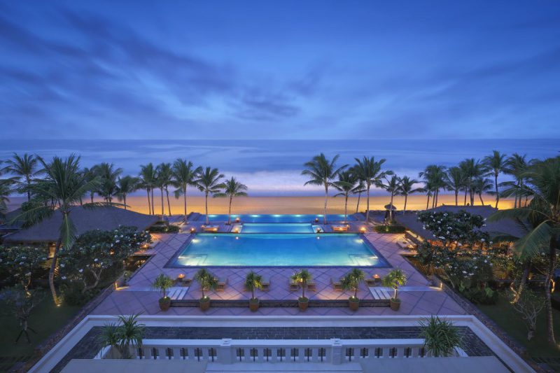 widok z balkonu hotelu na oświetlony ogórd z palmami i basenem, w tle plaża, Bali - Indonezja