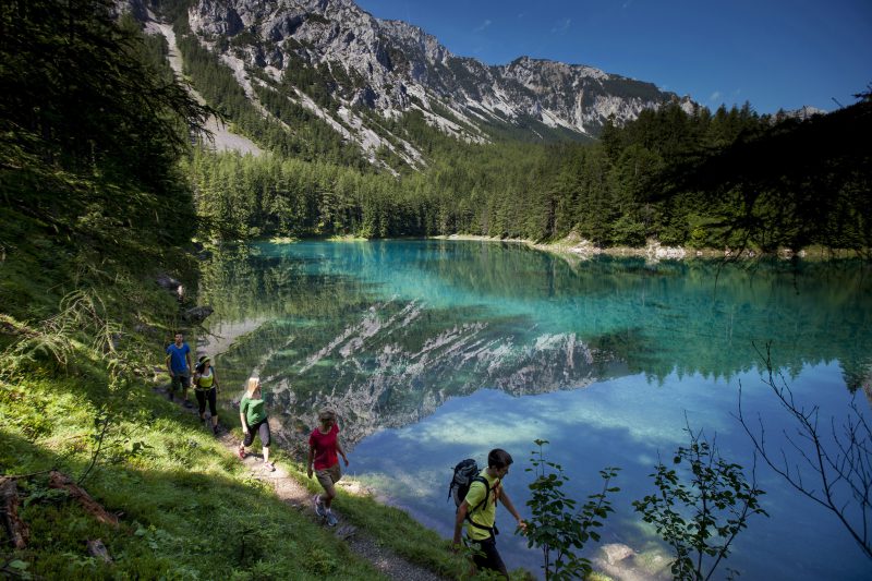 grupa turystów odbywająca pieszą wędrówkę, w tle błękitny staw i góry, Austria